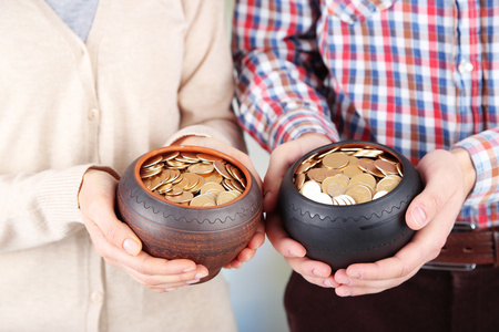 两个陶瓷罐与金币在男性和女性的手里，在明亮的背景上