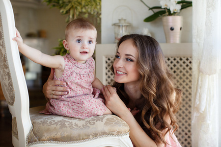 haome 在玩她的宝贝女儿近窗口内的快乐年轻吸引母亲的肖像。母亲和女儿的粉红色连衣裙