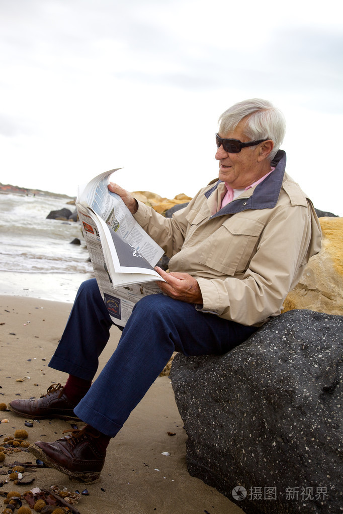 快乐老人读报纸在海滩上