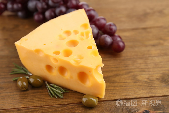 一块奶酪与绿色的橄榄,木制的背景上