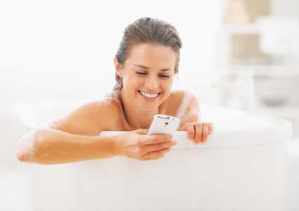 微笑的年轻女士发短信在浴缸里