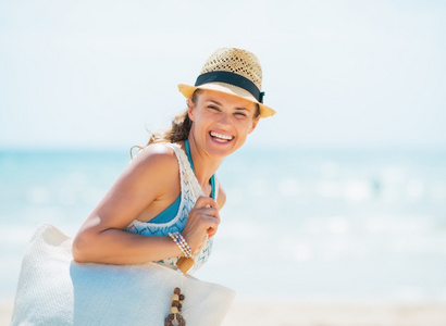 快乐的年轻女人，戴着帽子和带袋在海滩上的肖像