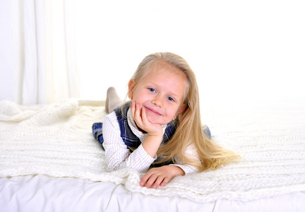 可爱的金发蓝眼睛的小女孩躺在床上的快乐