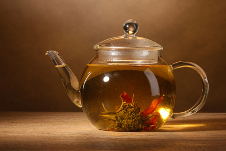 与异国情调绿茶棕色背景上的木桌上的玻璃茶壶