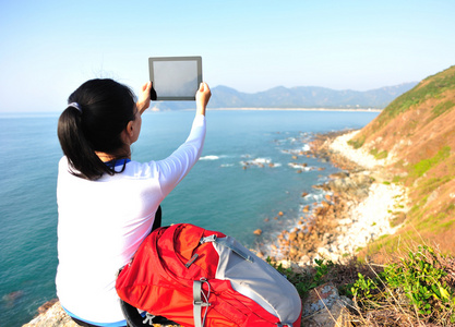 女人站在海边的岩石上，并使用数字平板电脑