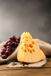 一块奶酪用葡萄和迷迭香在木桌子上，在深色背景上