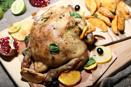 整个烤的鸡配蔬菜和烤的土豆上木板，木制的背景上