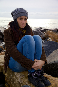可爱的年轻女子思想感情在面海的岩石上