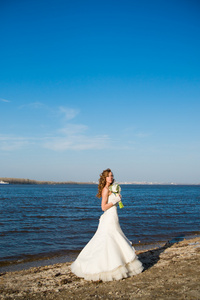 美丽的新娘穿着白色连衣裙海岸的河