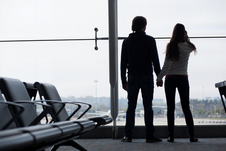 一对夫妇手牵着手，在机场候机楼等候的剪影
