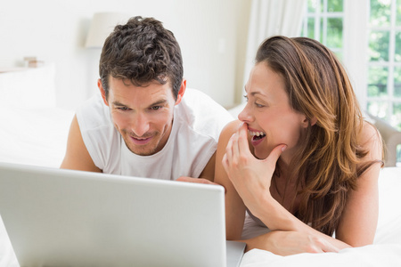 幸福的夫妻在床上使用笔记本电脑