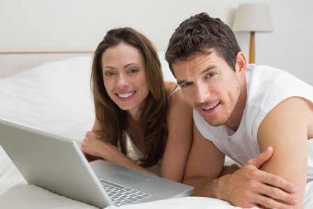 微笑着对夫妇在床上使用笔记本电脑