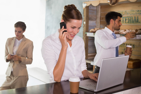 在公司的自助餐厅中使用移动电话和笔记本电脑的女商人