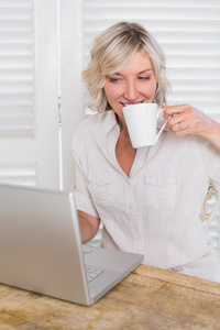 成熟的女人在使用笔记本电脑时喝咖啡