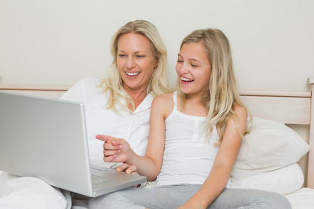 母亲和女儿一起在床上使用笔记本电脑