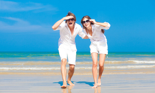 望着大海的沙滩上的白色行走对年轻快乐白种人夫妇前面观