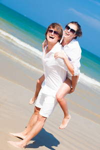 幸福的夫妇在墨镜和白色的衣服，在度假海滩上捎带开朗