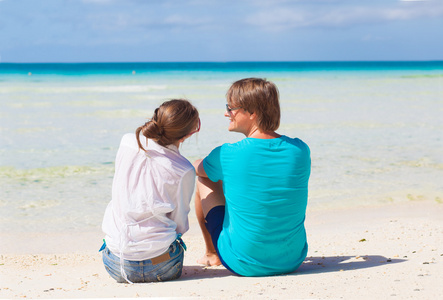 前面查看幸福的年轻夫妇在身鲜艳的衣服，坐在海滩上的太阳镜