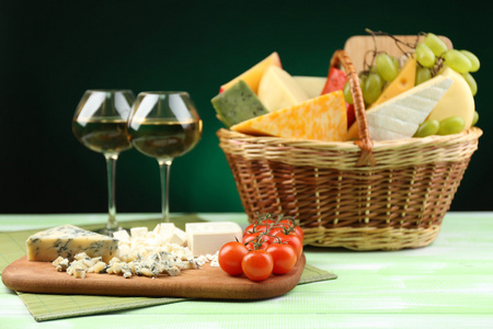 篮子里有不同的奶酪和葡萄酒的木桌前，在暗黑色背景上的眼镜