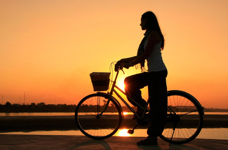 自行车在湄公河河滨水区在太阳的剪影的女人