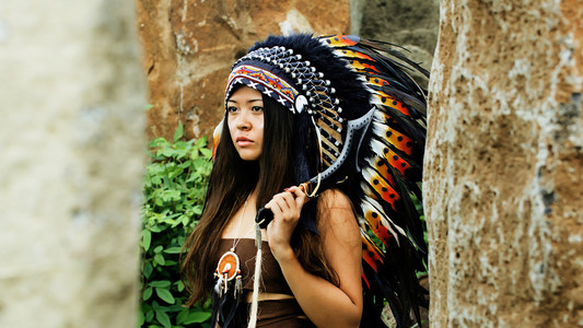 美洲印第安人，身穿传统服装与装饰的黑色斧头，站在两个石头之间