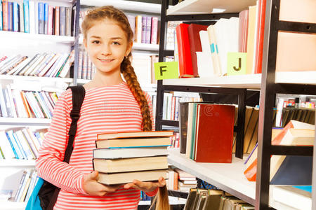 微笑的女孩拿着图书馆书架附近的书