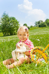 微笑的小女孩在绿色的草地上拥抱兔子