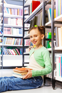 快乐的女孩拿着书坐在图书馆的地板上