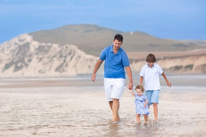 父亲带他的儿子和蹒跚学步的女孩走在沙滩上
