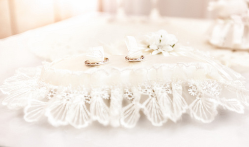 躺在白色的坐垫上的结婚戒指的照片