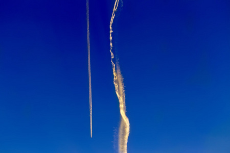 长长的拖尾的喷气式飞机在蔚蓝的天空照片