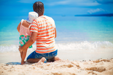 父亲带着小女儿放松在白色的沙滩上