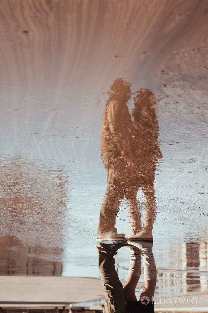 在水坑中的女人和男人在雨中伞下拥抱反射