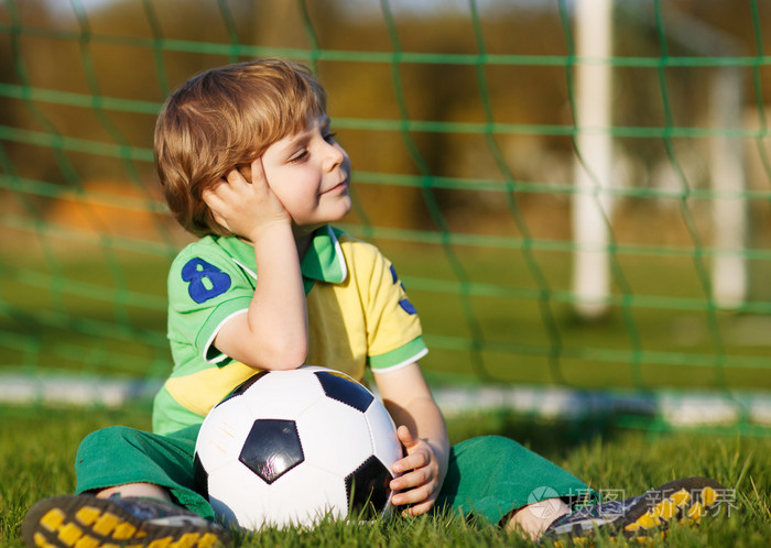 4在足球场踢足球和足球的金发男孩
