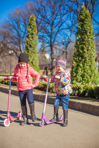 小可爱女孩与滑板车在春天公园在温暖的一天