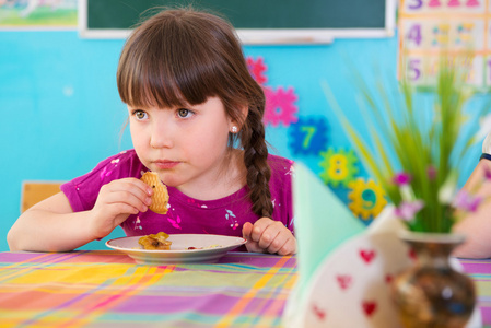 可爱的女孩在幼儿园吃烤的苹果图片
