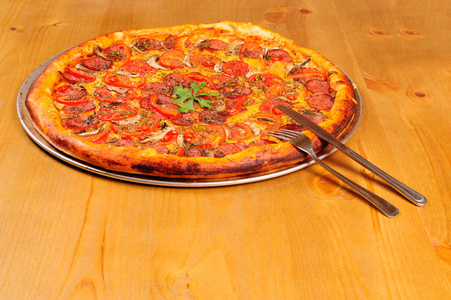 意大利辣香肠比萨饼用刀子和叉子木制的桌子上