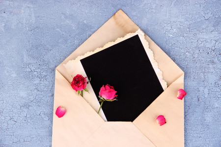 通过空白相纸和美丽的粉红色干的玫瑰木背景上的旧信封