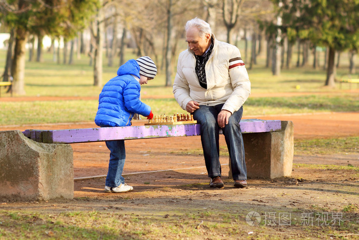 爷爷和孙子下棋在长椅上户外