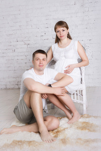 丈夫坐在地板上和怀孕的妻子接下来坐在椅子上