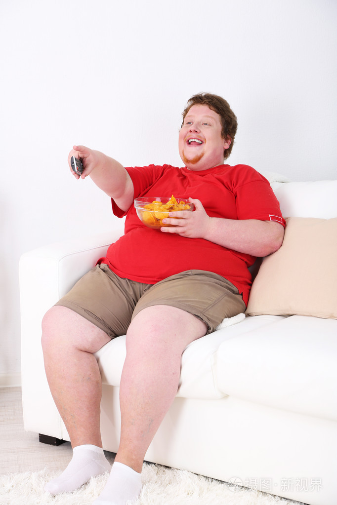 懒超重男性坐在沙发上，看电视