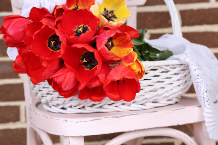 色彩艳丽的郁金香在柳条篮子里，在椅子上，对家庭室内背景的花束