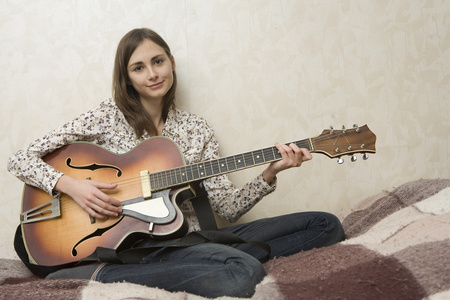 年轻漂亮的女人，在灰色的背景上弹吉他
