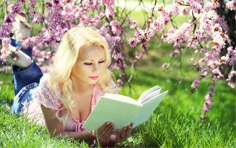 樱花下夹着本书的金发女人。漂亮女孩