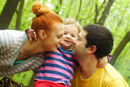 幸福的母亲和父亲亲吻他们的女儿在公园