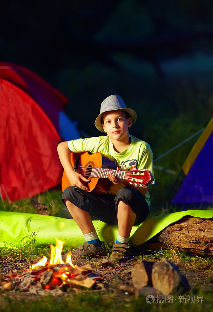 男孩弹着吉他附近篝火,夏令营