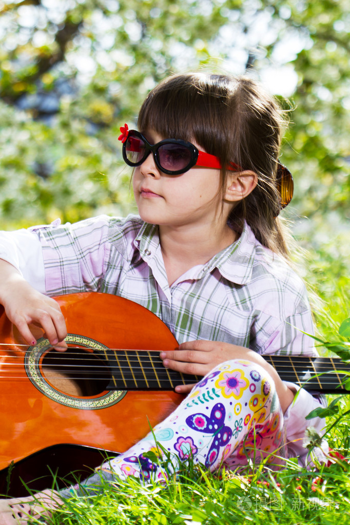 快乐的小女孩带着眼镜弹吉他户外
