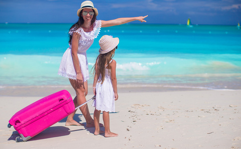 幸福的母亲和她的小女儿与热带的白色沙滩上的行李