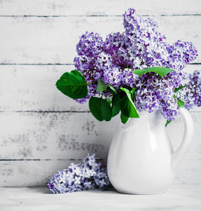 乡村背景上的白色花瓶中的紫丁香