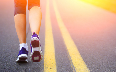 赛跑者女性的脚在道路上运行。慢跑